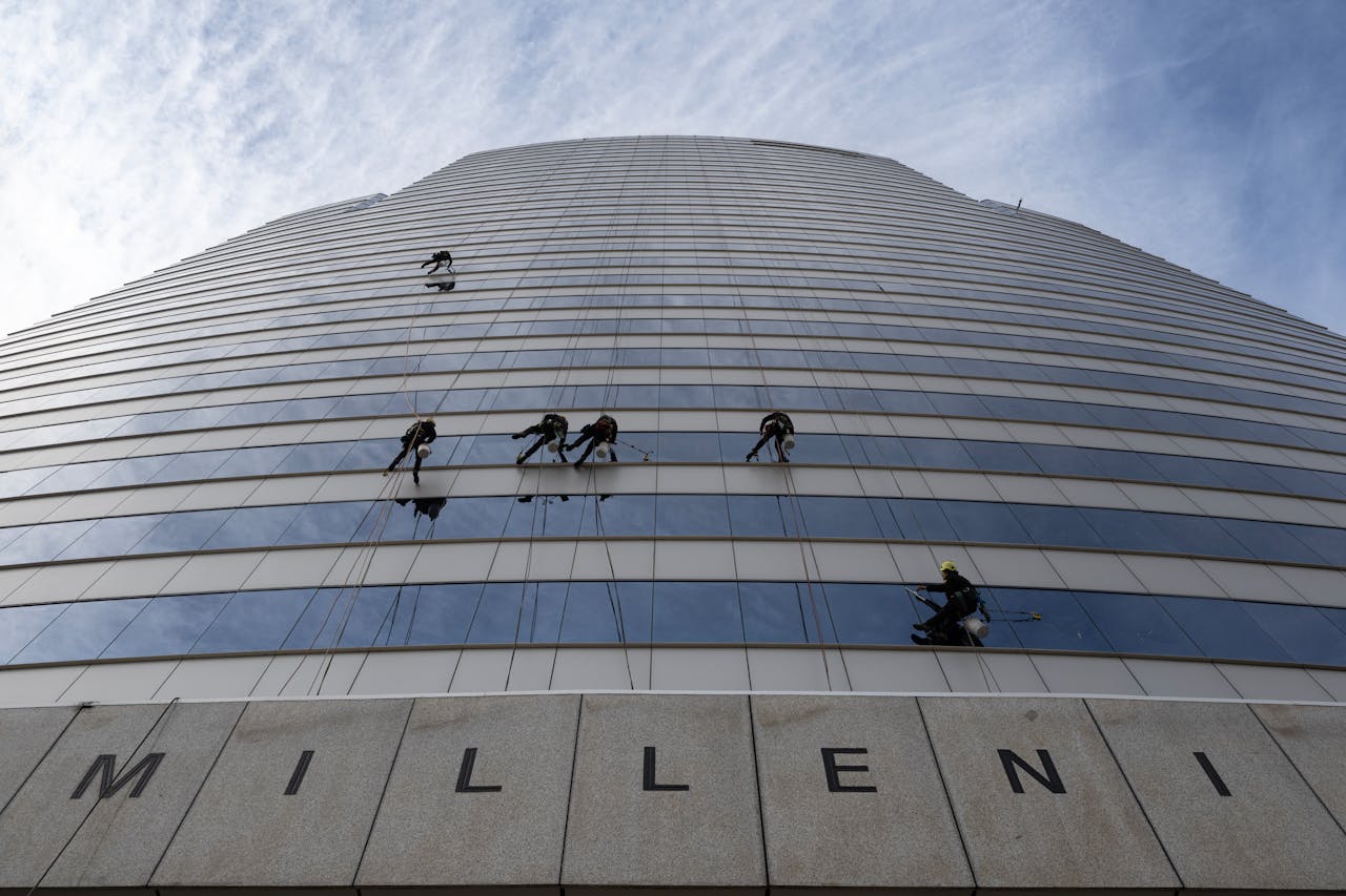 Services-03 Window cleaners suspended high up a Santiago skyscraper against a vibrant sky.